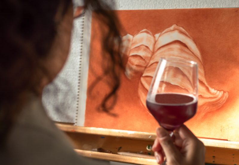 Woman holding a wine glass in front of a painting on an easel.