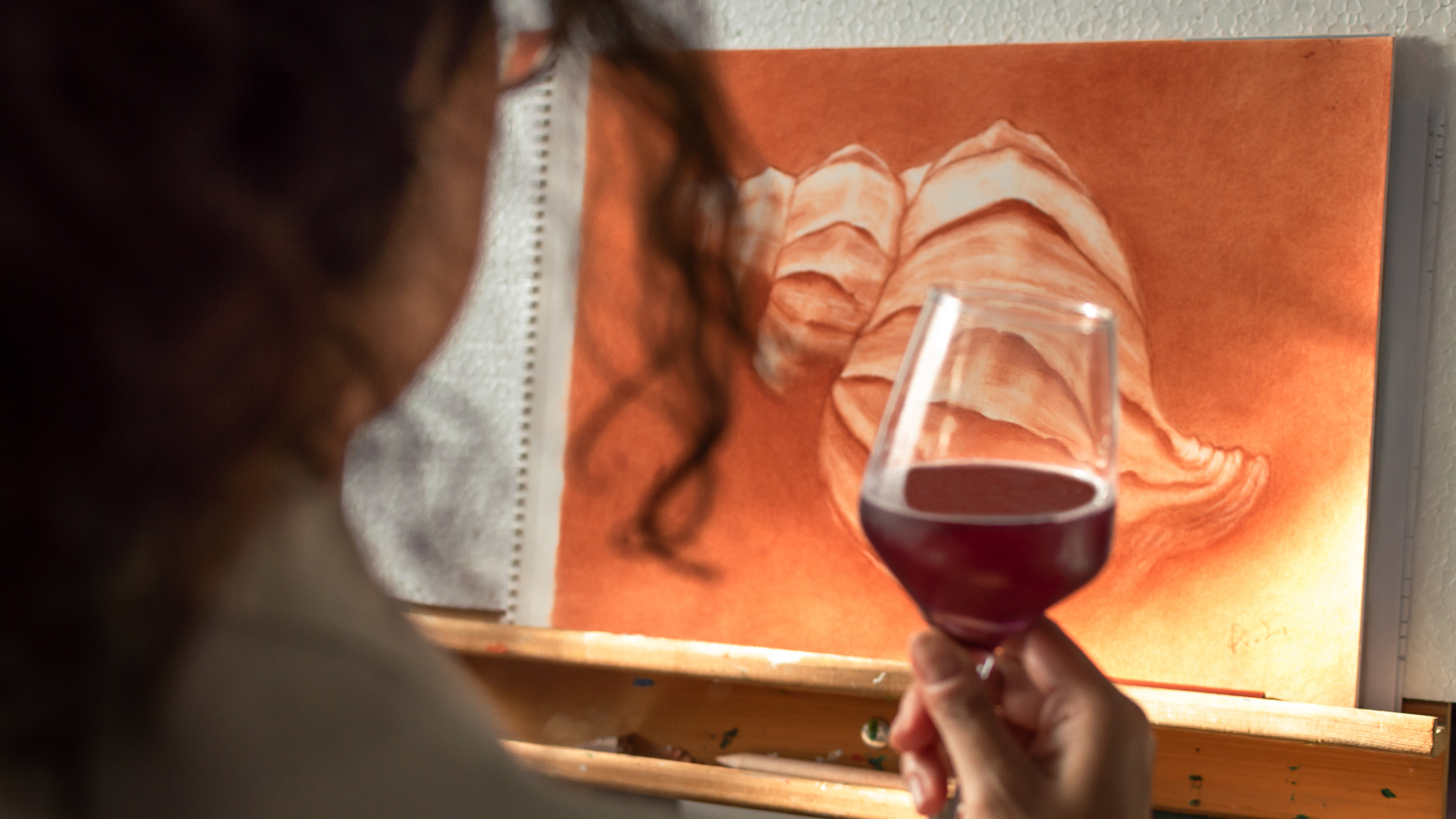 Woman holding a wine glass in front of a painting on an easel.